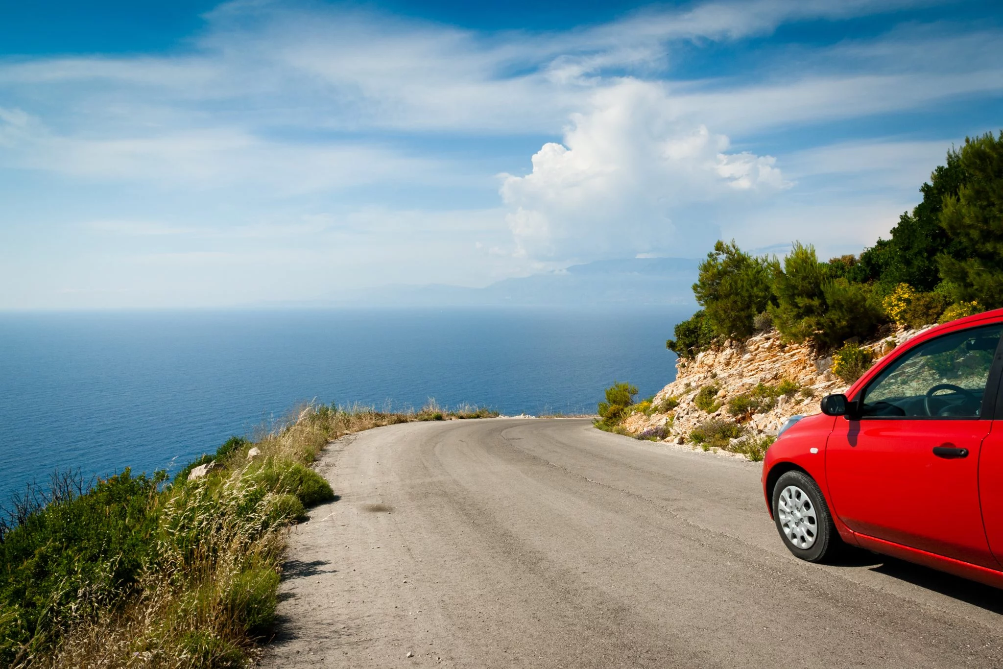 auto rossa su una stada secondaria con vista sul mare